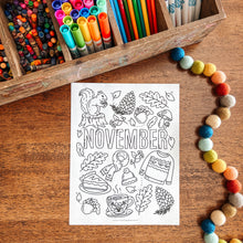 Load image into Gallery viewer, Coloring page with November-themed illustrations on a wooden surface with markers and beads.