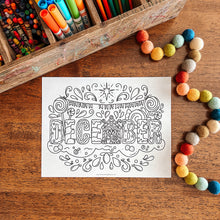 Load image into Gallery viewer, Coloring page with 'December' design on a wooden surface with art supplies.