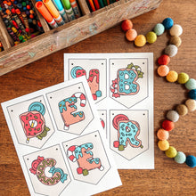 Load image into Gallery viewer, Colorful children's art supplies including markers, crayons, and a wooden box on a wooden surface with coloring sheets.