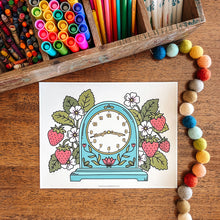 Load image into Gallery viewer, Coloring page with a clock design on a wooden surface with art supplies.