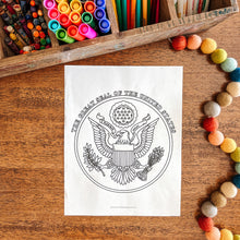 Load image into Gallery viewer, Coloring page with U.S. Great Seal surrounded by art supplies on a wooden surface