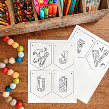 Load image into Gallery viewer, Colorful markers, crayons, and a wooden box on a wooden surface with June banner coloring sheets.