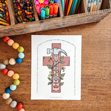 Load image into Gallery viewer, Coloring sheet with a cross design on a wooden surface with coloring supplies.