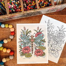 Load image into Gallery viewer, A coloring book or coloring page set displayed on a wooden table, with one page showing a colored dragonfly and lotus design and another page showing the black-and-white line art. A wooden box of colored pencils and a string of colorful pom-poms are arranged around it.