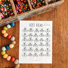 Load image into Gallery viewer, A children's reading activity sheet featuring black line drawings of moths and moths with the text 'LET'S READ' at the top, placed on a wooden table next to a wooden pencil tray and colorful beads.