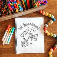 Load image into Gallery viewer, Notebook with a drawing of the First Amendment on a wooden surface with art supplies.
