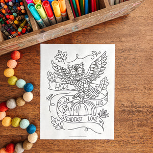 Coloring sheet with owl design on a wooden table with art supplies