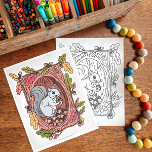 Coloring pages with a squirrel design, markers, and pom-poms on a wooden surface