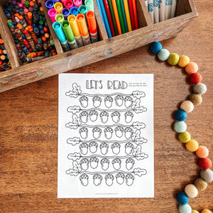 Colorful markers in a wooden box with a coloring sheet titled 'Let's Read' on a wooden surface.