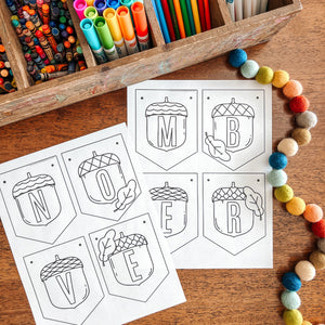 Colorful markers in a wooden box with November banner coloring sheets on a wooden surface.