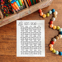 Load image into Gallery viewer, Coloring sheet with gingerbread men design on a wooden surface with art supplies.
