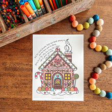 Load image into Gallery viewer, Coloring page of a gingerbread house on a wooden surface with coloring supplies.
