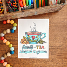 Load image into Gallery viewer, Colorful stationery items including markers, crayons, and colored pencils in a wooden box on a wooden surface with a 'Tea Steeped in Grace' print.
