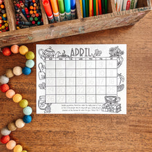Load image into Gallery viewer, April calendar on a wooden surface with colorful stationery items.
