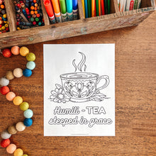 Load image into Gallery viewer, Coloring book page with a tea cup design on a wooden surface with art supplies.
