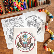 Load image into Gallery viewer, Coloring pages with United States Great Seal, markers, and coloring sheets on a wooden surface.
