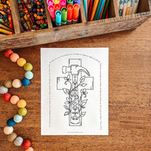 Load image into Gallery viewer, Colorful markers, crayons, and a coloring page of a cross with flowers on a wooden surface.

