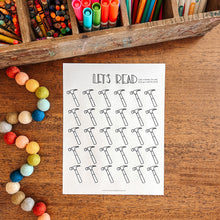 Load image into Gallery viewer, Colorful markers and crayons in a wooden box on a wooden surface with a 'Let's Read' worksheet.
