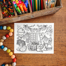 Load image into Gallery viewer, Coloring page with July-themed illustrations on a wooden surface with art supplies.
