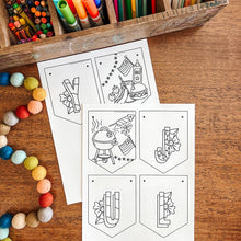 Load image into Gallery viewer, Coloring supplies including markers, pencils, and coloring July banner on a wooden surface.

