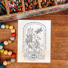 Load image into Gallery viewer, A black-and-white printable coloring page featuring a duck family, lily pads, reeds, and a dragonfly, placed on a wooden tabletop with crayons and colorful beads nearby.
