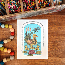 Load image into Gallery viewer, An art print featuring a duck family illustration with the Bible verse Psalm 23:1-3 printed around the border, displayed on a wooden tabletop surrounded by colorful art supplies and pom-poms.
