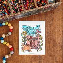 Load image into Gallery viewer, A printed Thanksgiving-themed art card featuring a colorful illustration of a barn gate, pumpkins, sunflowers, and a bird, placed on a wooden tabletop with a box of colored pencils and multicolored beads nearby.
