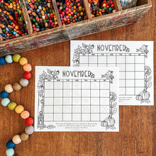 Load image into Gallery viewer, Two printable November planner pages with autumn-themed black line art are displayed on a wooden table alongside a wooden pencil box and colorful beads.

