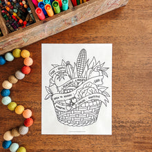 Load image into Gallery viewer, Coloring sheet with a basket of vegetables on a wooden surface with art supplies.
