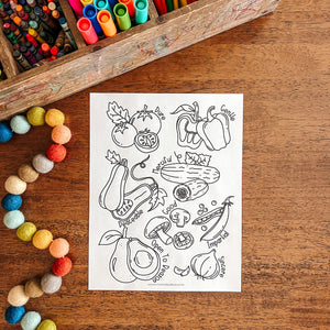 Coloring sheet with vegetable illustrations on a wooden table with art supplies.
