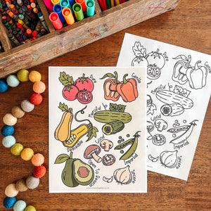 Coloring sheets with vegetable illustrations on a wooden surface with art supplies.